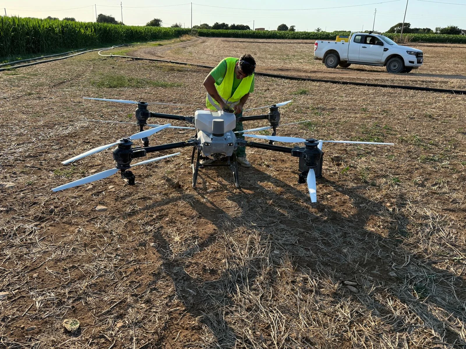 Un operatore con gilet ad alta visibilità prepara il drone agricolo a terra prima dell’intervento.